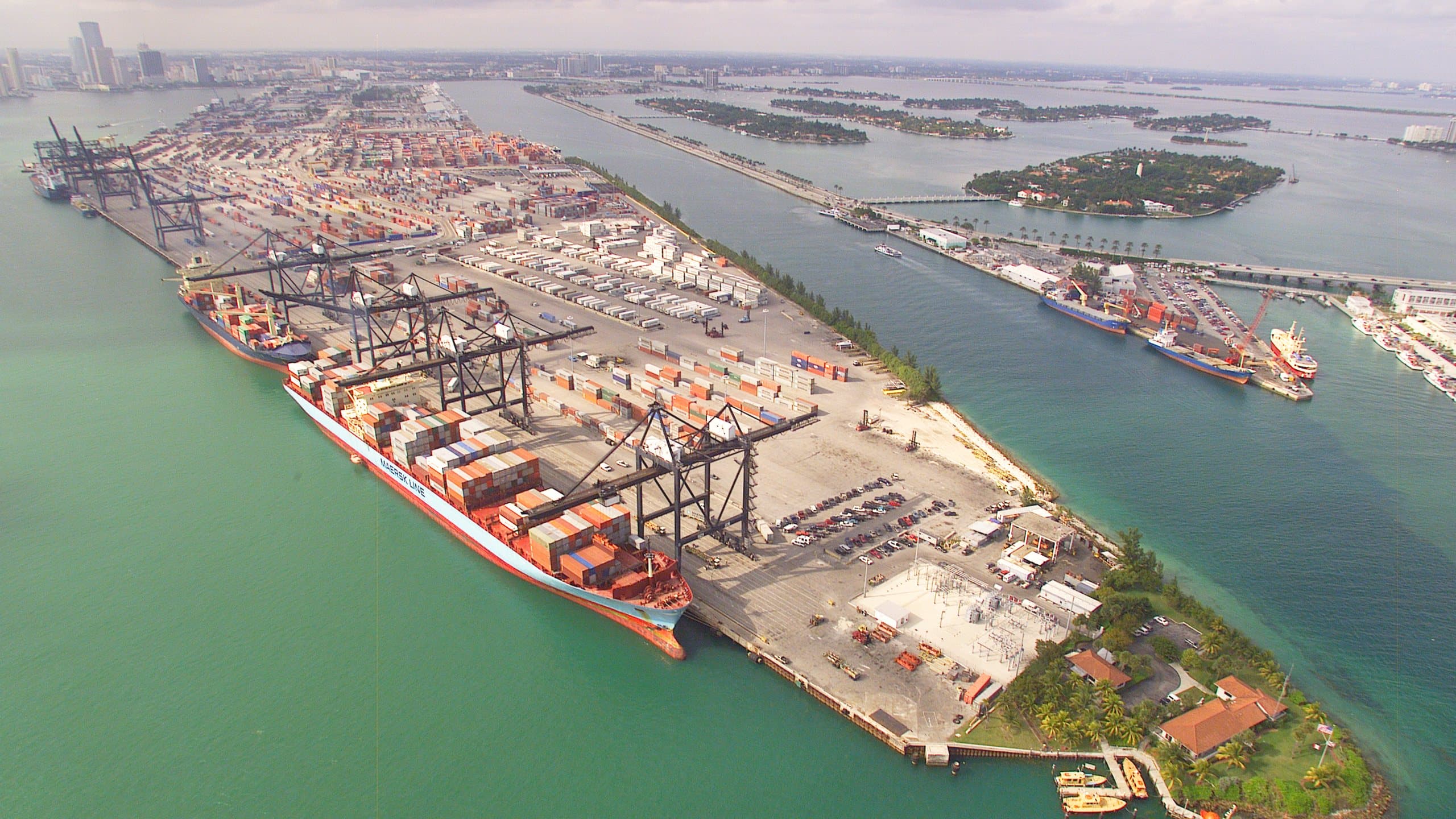 Vista aérea de una terminal portuaria con contenedores y grúas junto al agua.